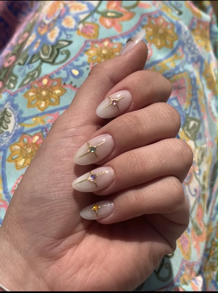 Milky almond nails with a gold star and a coloured gem on each finger